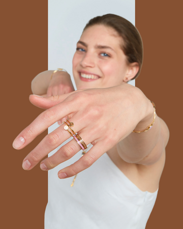 A smiling woman wearing a prominent Jason Hyde multi-band gold and pink ring, with other delicate j