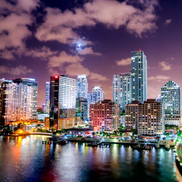 A nighttime photo of the Miami skyline with city lights reflecting on the water.