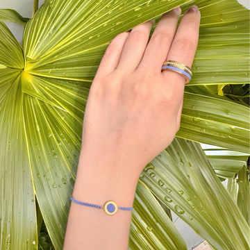 A hand wearing lavender jewelry, resting on a green leaf.