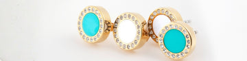 Close-up of four gold circular earrings or charms, two with turquoise centers and two with white centers