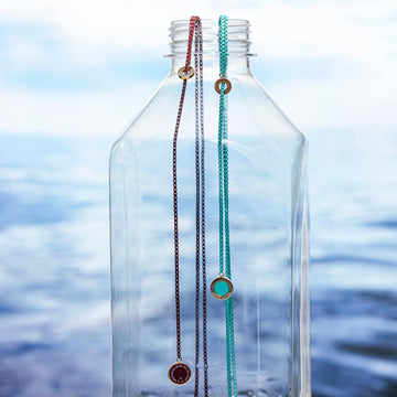 Sustainable necklaces in turquoise and red on top of bottle