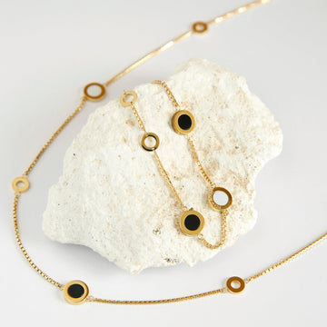 Gold necklace with black and white chips displayed on a white stone