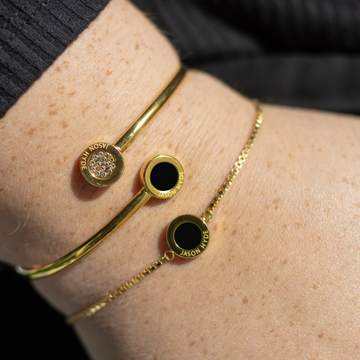 Woman’s wrist wearing two Jason Hyde gold bracelets with black enamel accents