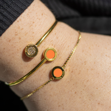 Close-up of a woman’s wrist wearing two Jason Hyde gold bracelets with orange enamel accents