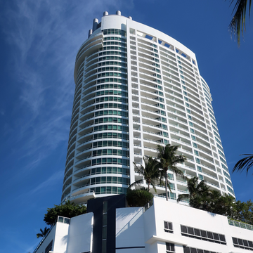 Modern white building with curved balconies and green windows under blue sky
