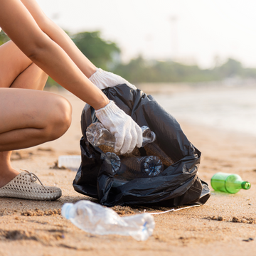 Person wearing gloves collecting plastic bottles and trash on a sandy beach