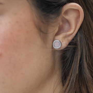 Close-up of an ear wearing a round silver stud earring with a light pink chip