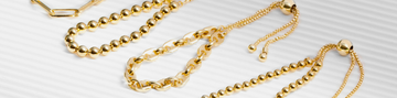 Close-up of assorted gold chain bracelets on a textured white surface.