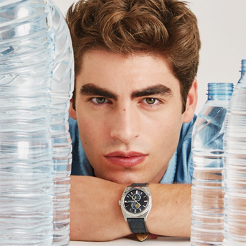 Man modeling a silver watch with a dark dial and black strap.