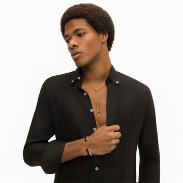 A man wearing a black shirt, a gold cross necklace, and a silver and black bangle bracelet.