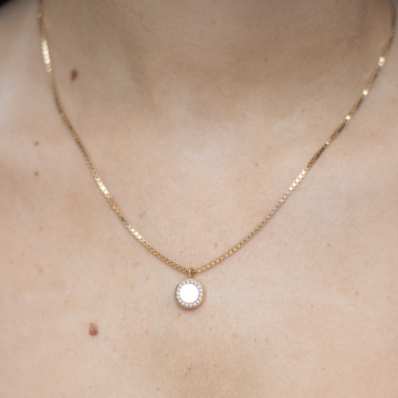 Delicate gold necklace featuring a white chip pendant encircled with zirconia