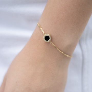 Gold bracelet with a round black chip surrounded by sparkling white zirconia