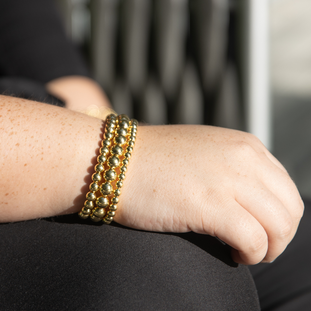 Close-up of Jason Hyde 'CATENE' collection gold plated beaded bracelets stacked on a wrist