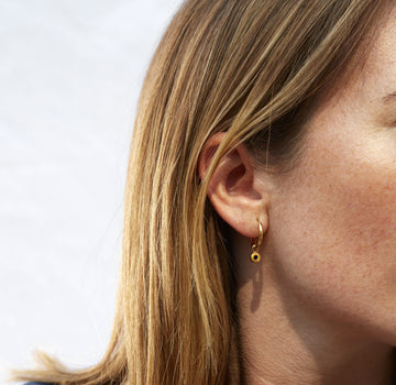 Gold hoop earring with black charm worn on a woman’s ear