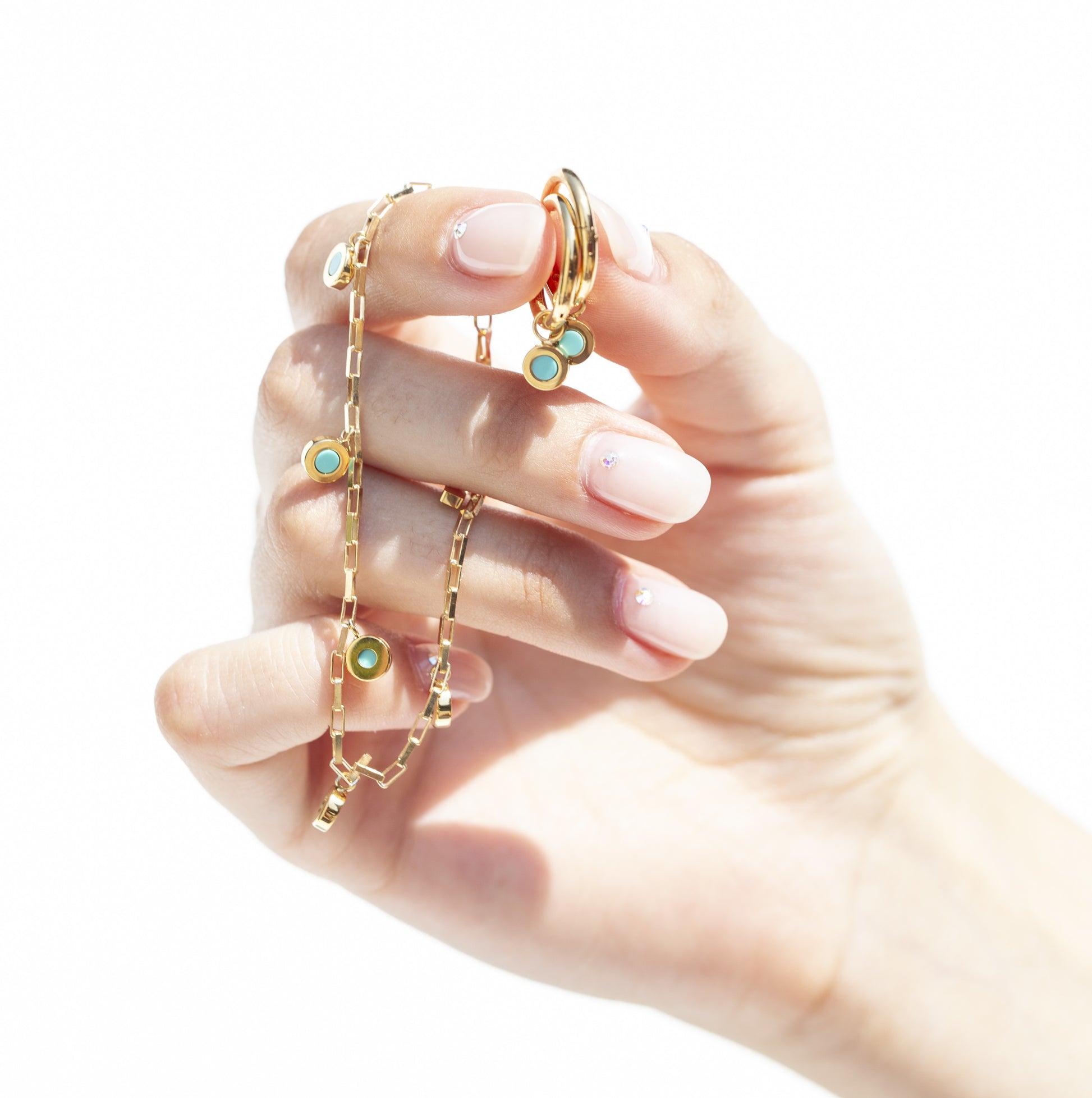 Gold chain and earrings with turquoise ocean plastic charms held by manicured hand