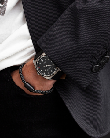 Close-up of a man's wrist wearing a silver-toned watch with a black braided cord bracelet