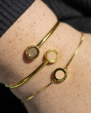Close-up of a wrist wearing two layered gold-tone Jason Hyde bracelets