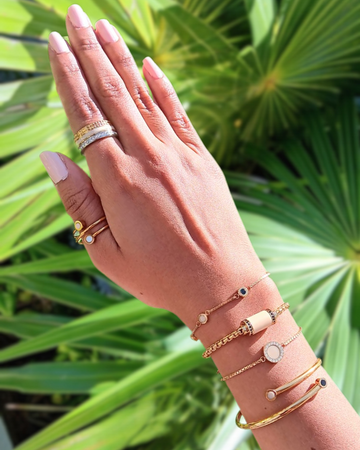 Close-up of a person's hand wearing a mix of Jason Hyde gold-tone beige jewelry