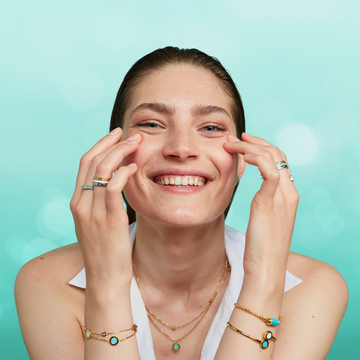 Woman smiling and touching her face, showcasing a variety of Jason Hyde turquoise and gold jewelry