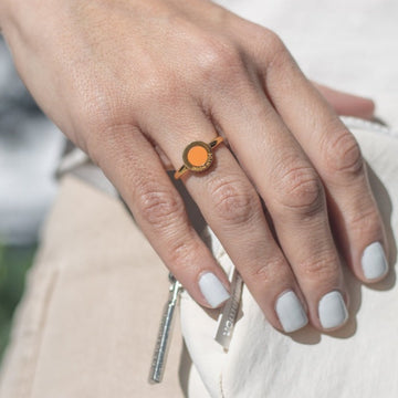 Hand wearing a gold Jason Hyde ring with an orange chip