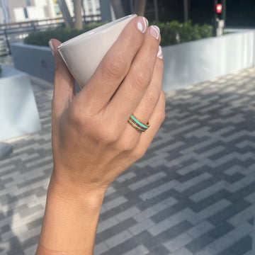 Close-up of hand holding cup, adorned with Jason Hyde gold ring featuring turquoise enamel
