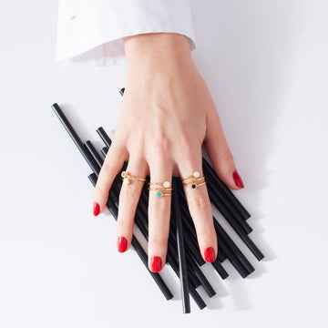 A hand with red nail polish wearing several gold rings