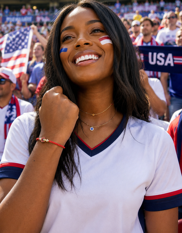Two gold necklaces one with a blue charm and a red bracelet on a woman in a white USA soccer jersey
