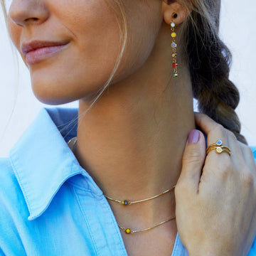 Gold tone earrings with colorful charms matching layered necklaces and two stacked rings with round charms