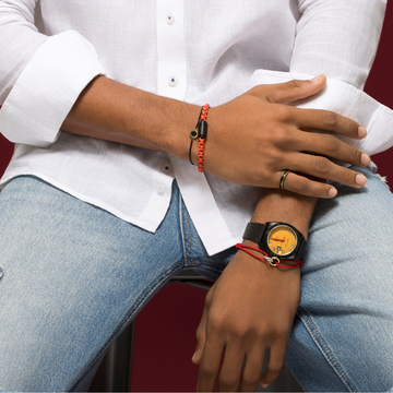 Close-up of a man wearing a black watch with a yellow dial, red cord bracelet, orange bracelet, and ring in white shirt.