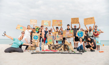 Diverse group of people on a beach holding environmental signs and a pile of collected trash