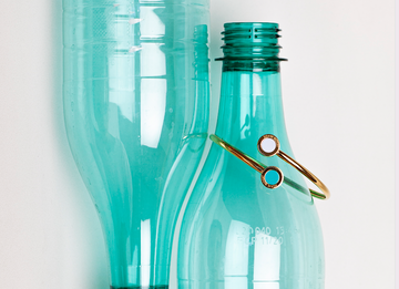 Gold cuff bracelet with white and turquoise enamel dots resting on a teal plastic bottle
