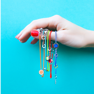 A female hand with red nail polish holding multiple Jason Hyde colorful chain bracelets
