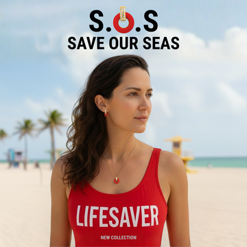 Model wearing 'LIFESAVER' red swimsuit, red enamel necklace and earrings with S.O.S Save Our Seas text on a sunny beach.