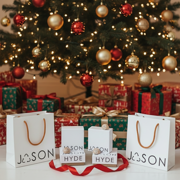Jason Hyde jewelry gift bags and boxes with a red ribbon in front of a Christmas tree and wrapped gifts