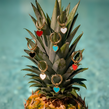 Gold hoop earrings with heart-shaped charms in red black white and turquoise displayed on a pineapple