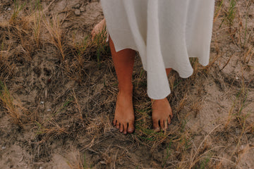 Bare feet on dirt with dried grass white fabric covering legs