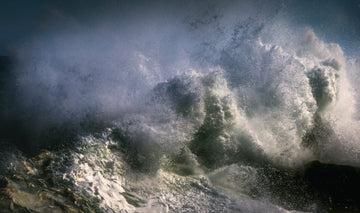 Massive ocean wave crashing spraying white foam and dark water against a stormy sky