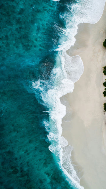 Aerial view of a white sandy beach with turquoise ocean water and white crashing waves