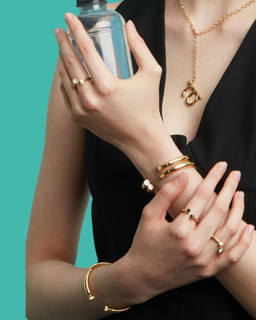 A woman, accessorized with a curated collection of modern gold rings and bangles