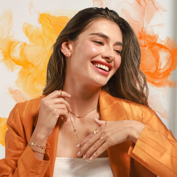 A smiling woman in an orange blazer wearing layered jewelry