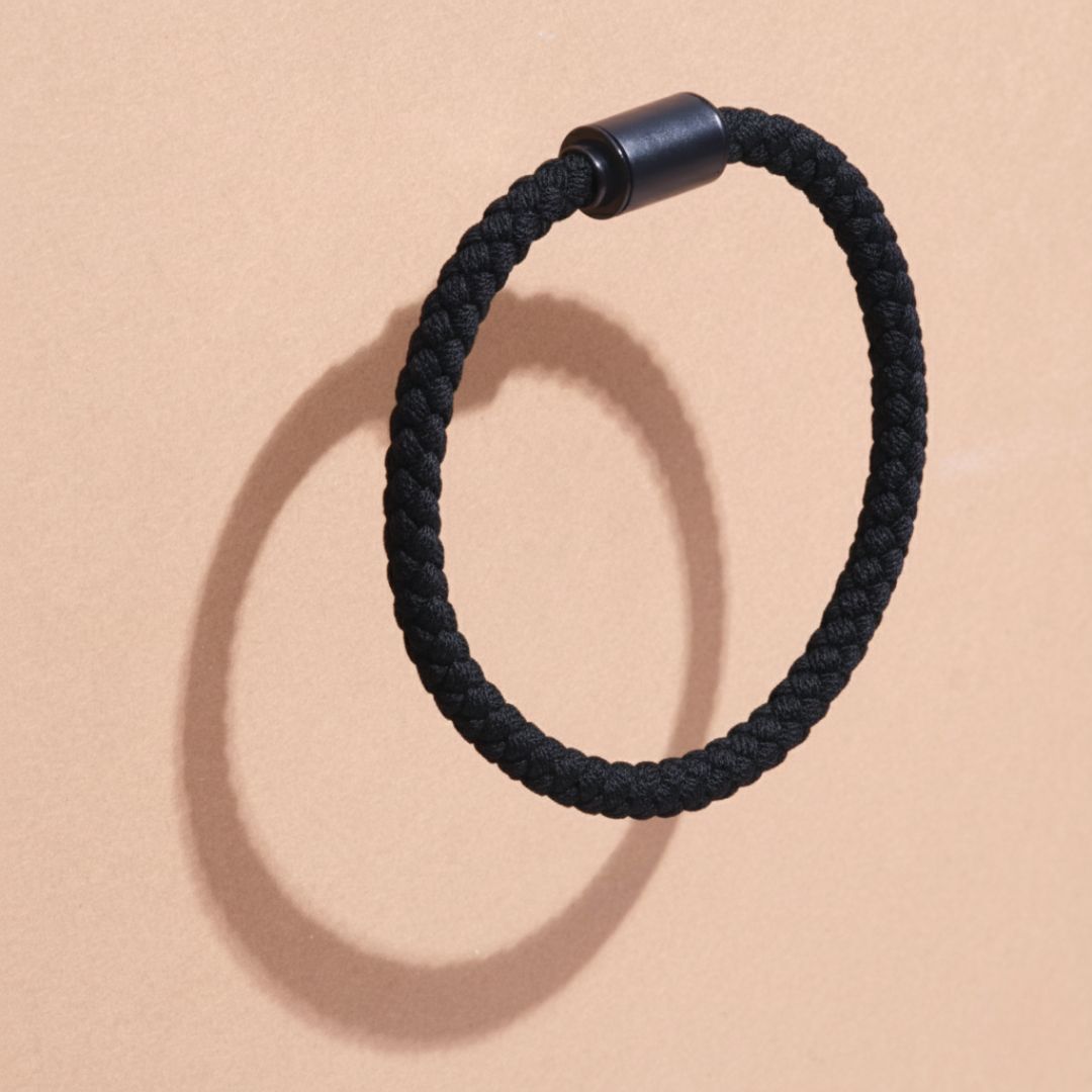Minimalist black rope bracelet floating above a tan surface.