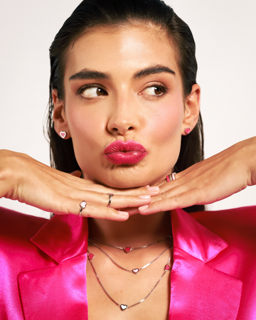 Woman blowing kiss wearing Amare earrings, rings and necklaces in pink and raspberry