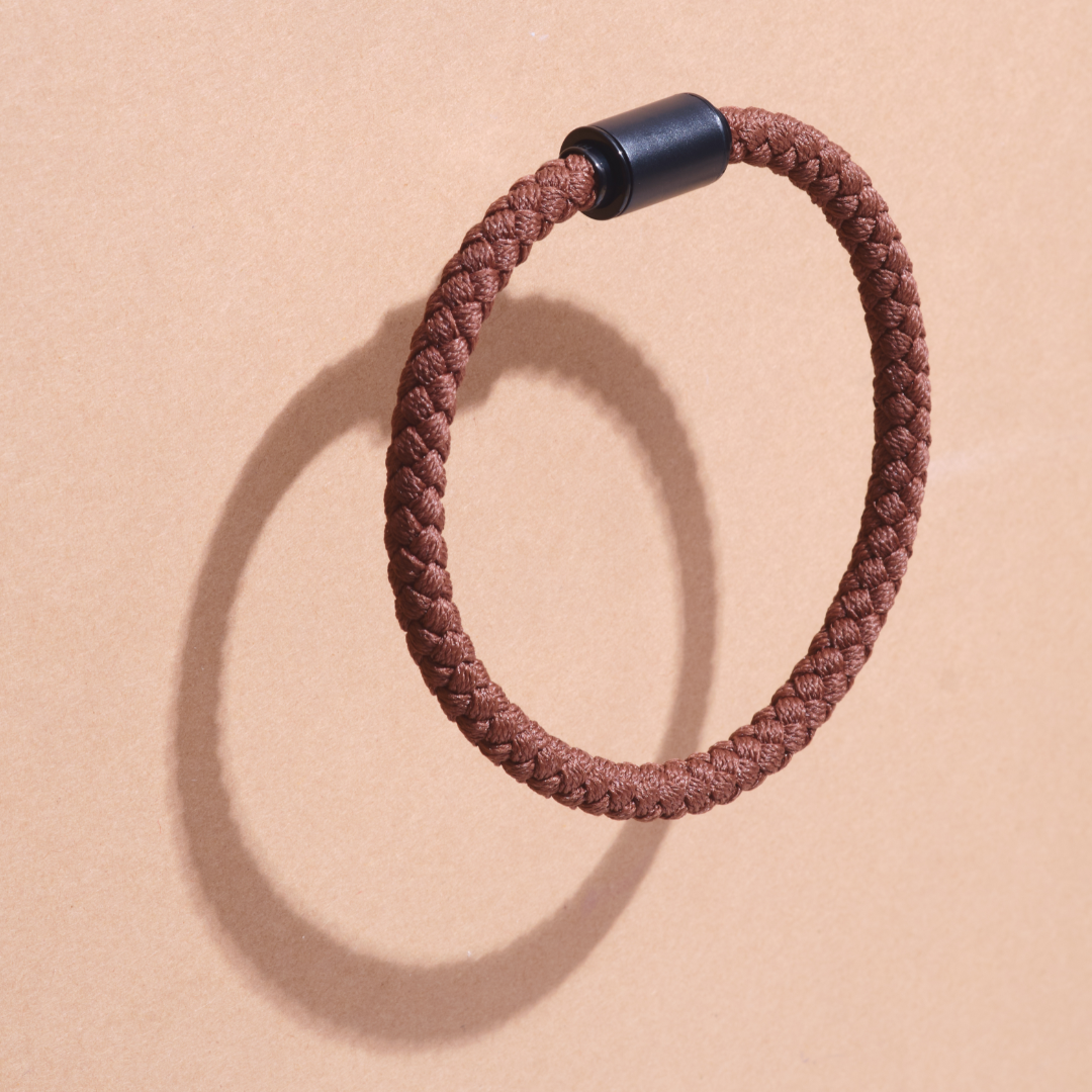 Brown rope bracelet floating above a tan surface.