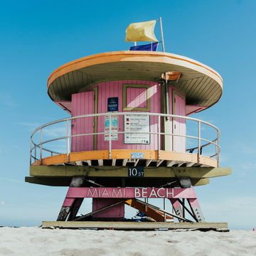 A vibrant pink lifeguard tower with a yellow flag, located at 10th Street on Miami Beach
