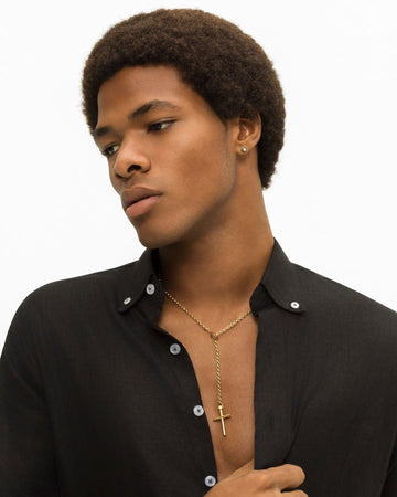 Young man with an afro, wearing an open black shirt and a gold cross necklace.