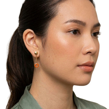 Model wearing a Jason Hyde gold stud earring with a dangling recycled orange plastic hoop.
