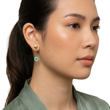Woman wearing a Jason Hyde gold stud earring with a dangling recycled turquoise plastic hoop.