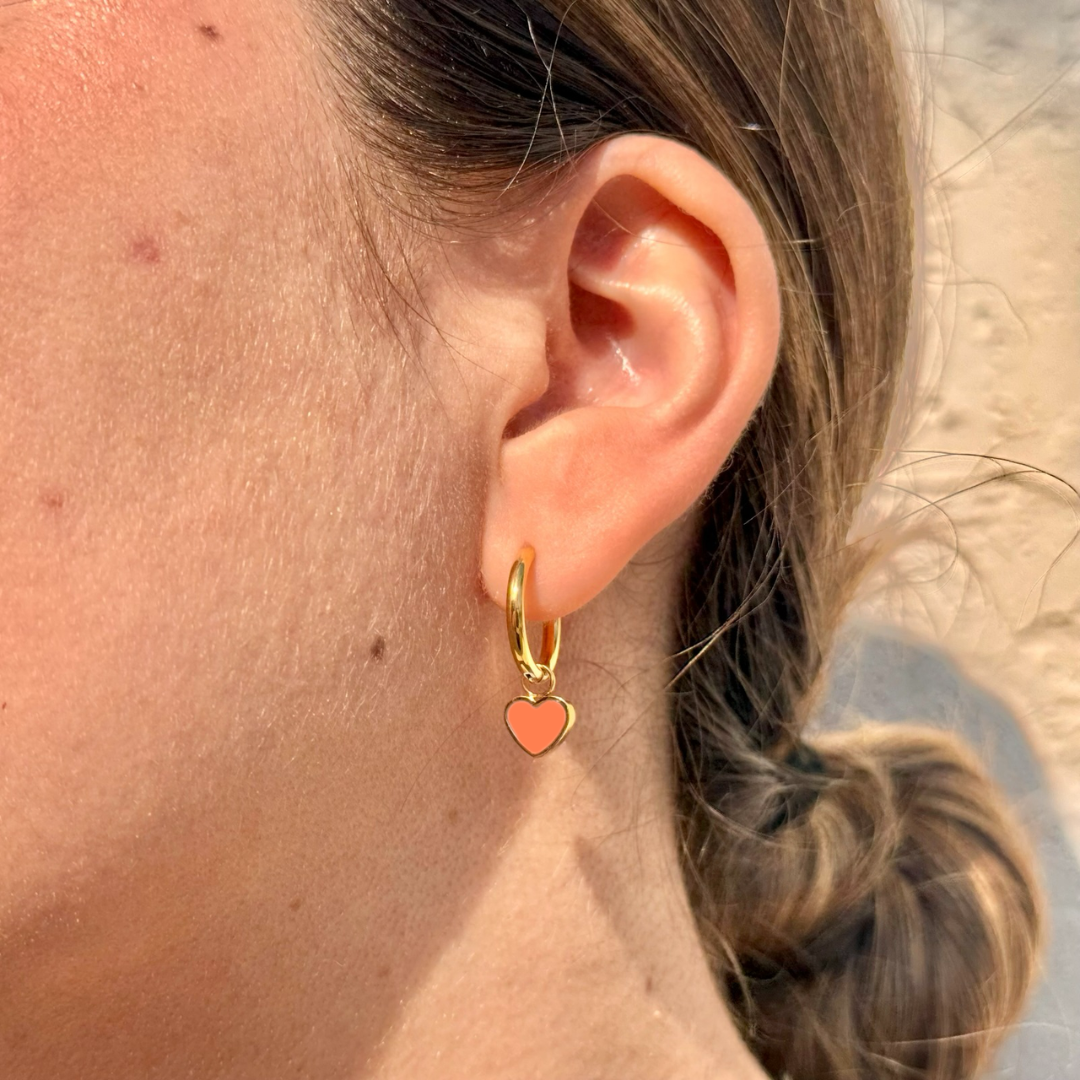 Woman wearing Jason Hyde gold hoop earrings with coral heart charms in a modern everyday look.