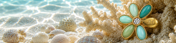 Gold flower charm with turquoise petals and a zirconia center resting on white coral underwater over a sandy seabed.
