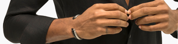 Close-up of a man's wrist wearing stacked silver and black metal cuff bracelets with a black linen shirt